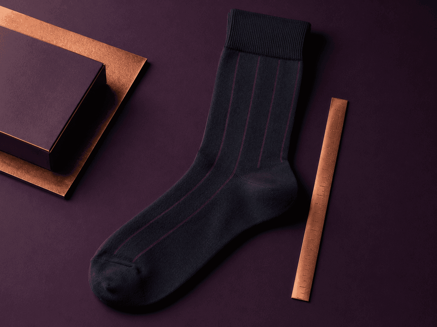 A fine-knit dress sock lying next to a slim measuring rule
